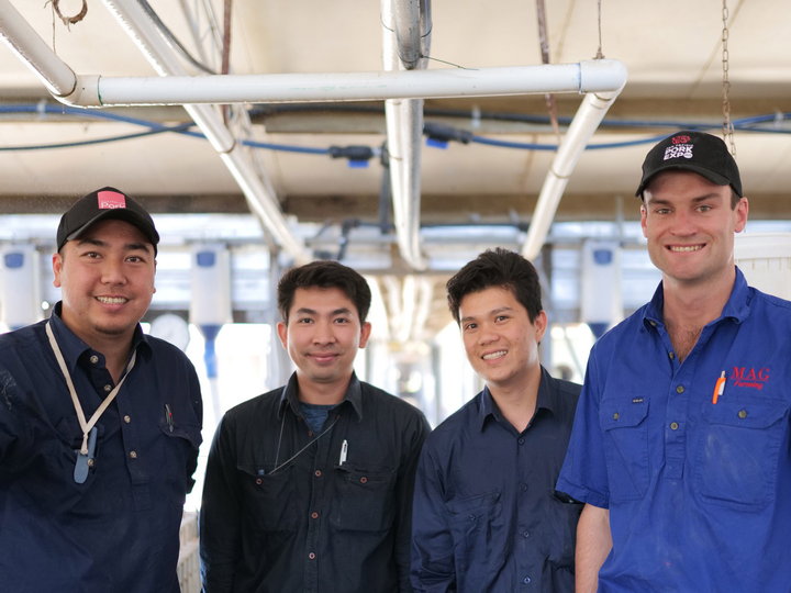 Farmer wearing blue shirt standing with three overseas workers wearing navy blue shirts. All smiling at camera.