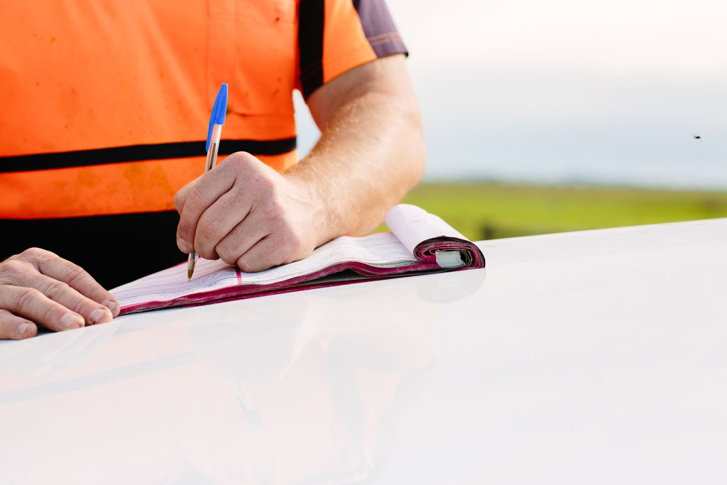 Man writing on notepad on bonnet of car