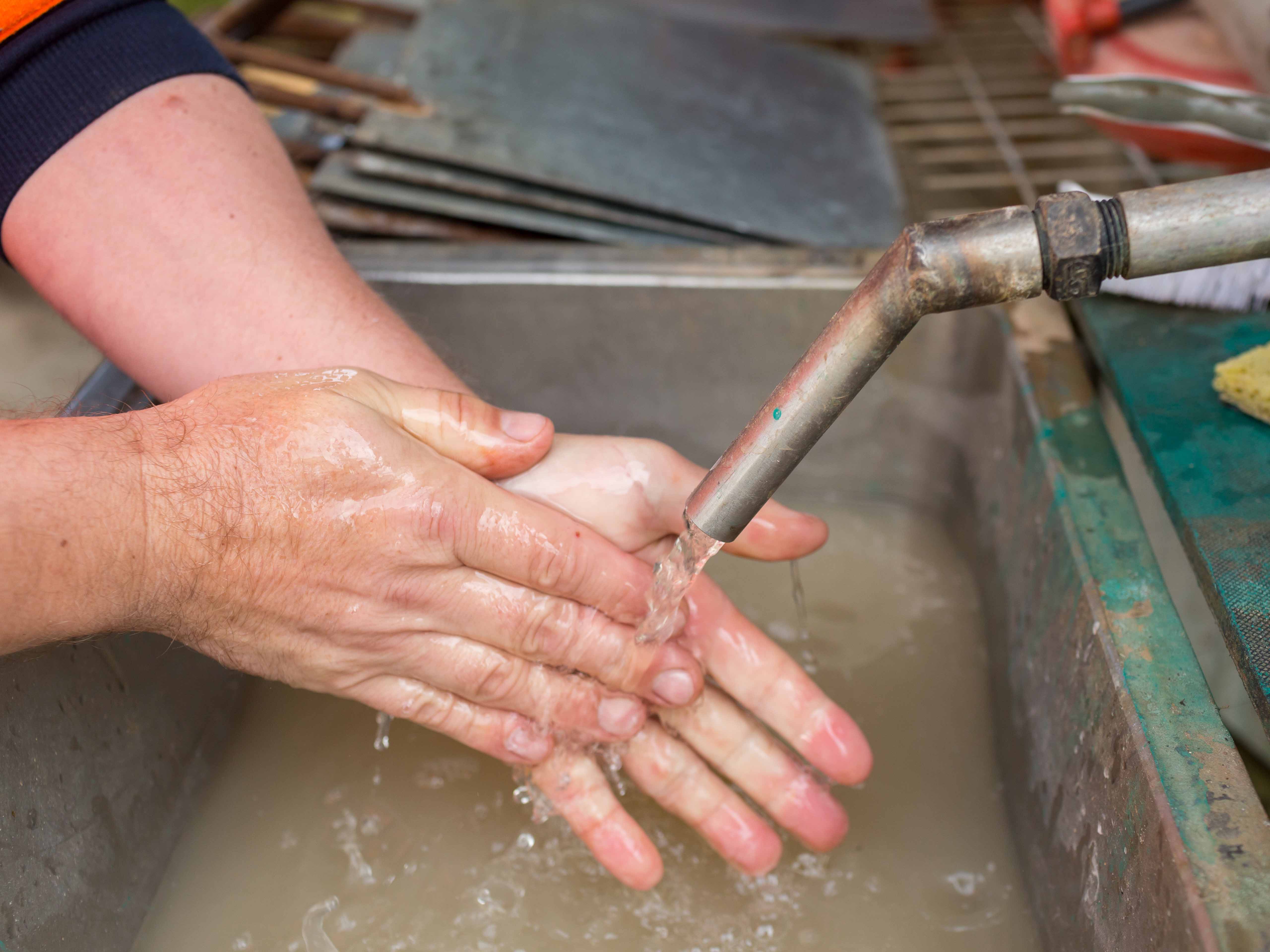 Close up of man washing hands in running water. Water falling into sink below hands.